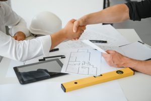 Construction professionals reviewing plans and shaking hands during a construction handover
