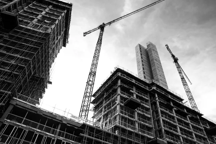A black and white image of a crane towering over an office block construction.