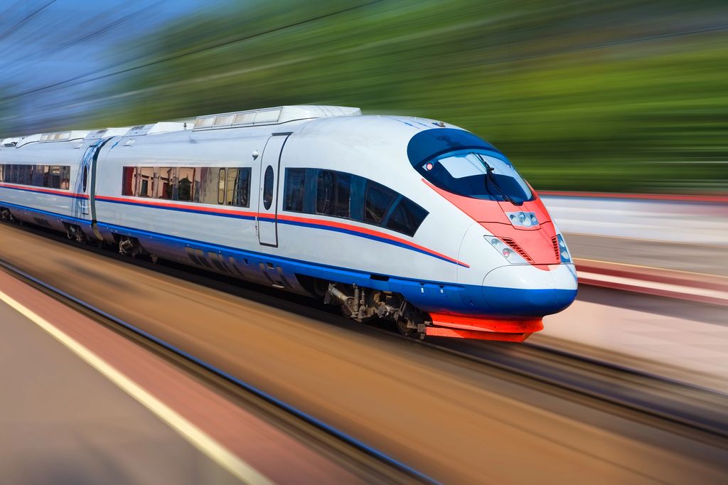 High-speed train in motion, captured with a motion blur effect to emphasize speed, with the train's sleek white, blue, and red design sharply contrasted against the blurred greenery in the background.
