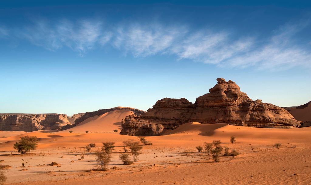Desert landscape at the Great Man-Made River project in Libya, featuring rolling sand dunes, distinctive rock formations, and scattered greenery under a vast blue sky.
