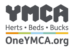 Logo of YMCA for Hertfordshire, Bedfordshire, and Buckinghamshire regions, featuring bold 'YMCA' letters in grayscale above the tagline 'Herts • Beds • Bucks'. A colorful horizontal stripe is present beneath the text and the website 'OneYMCA.org' is displayed at the bottom.