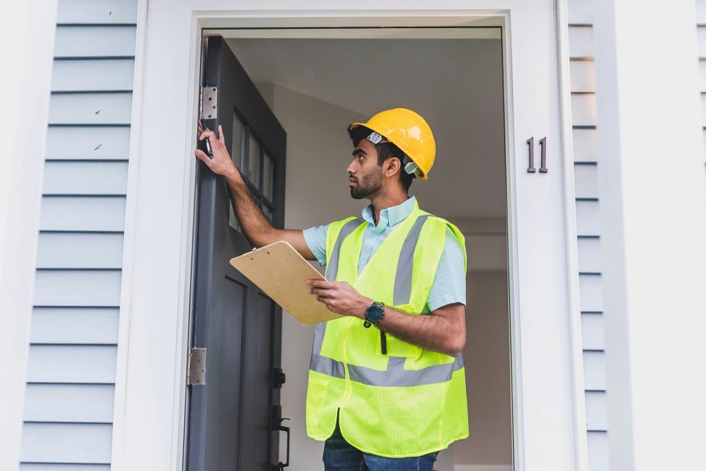 Housing inspector checking door frame with clipboard during property inspection