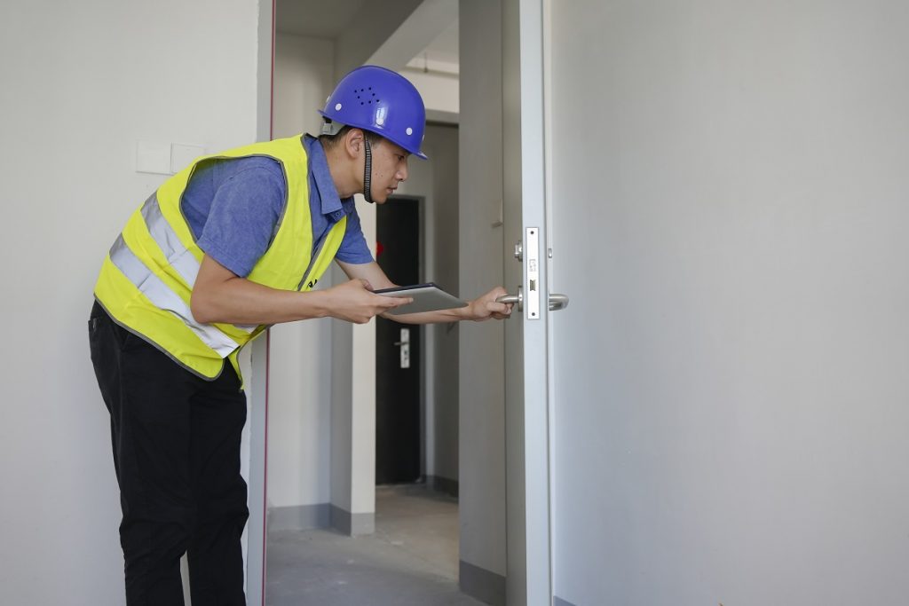 Engineer inspecting fire door using tablet for compliance documentation