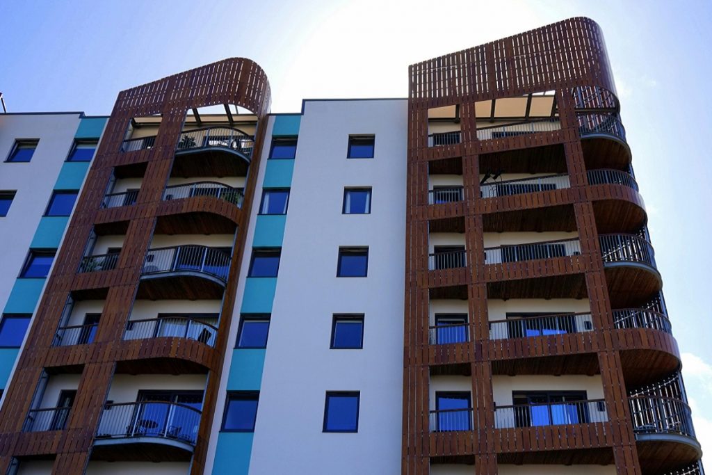 Modern UK social housing apartments with balconies, viewed from below against a clear sky